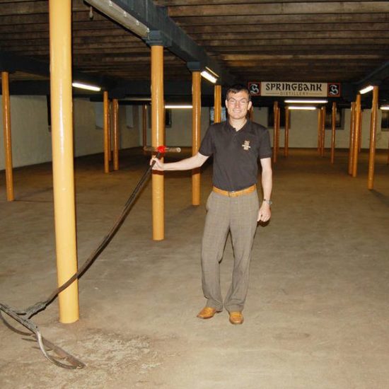 Mann mit Rechen auf einem leeren Malting Floor der Springbank Distillery.