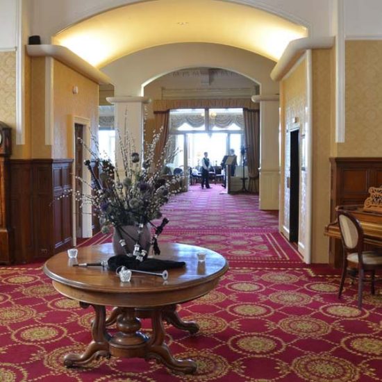 Großzügige Lobby eines Hotels mit rotem Teppichboden, rundem Tisch und Flügel.