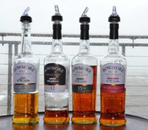 Vier Flaschen von Bowmore vor einer regennassen Scheibe und grauem Meer.