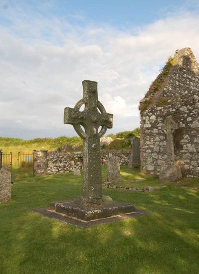 Keltisches Hochkreuz steht auf einem alten Friedhof mit Ruine einer Kapelle.