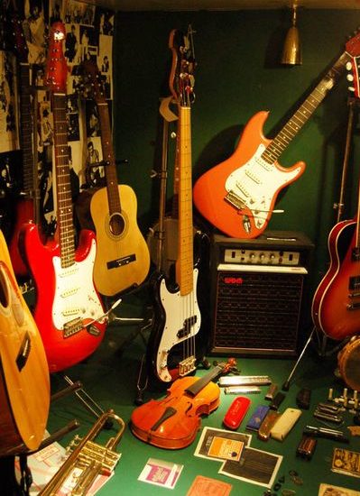 Sechs Gitarren, eine Trompete, eine Geige und Mundharmonikas sind zusammen mit Fotos und einem Verstärker in einem grün tapezierten Schaukasten präsentiert.