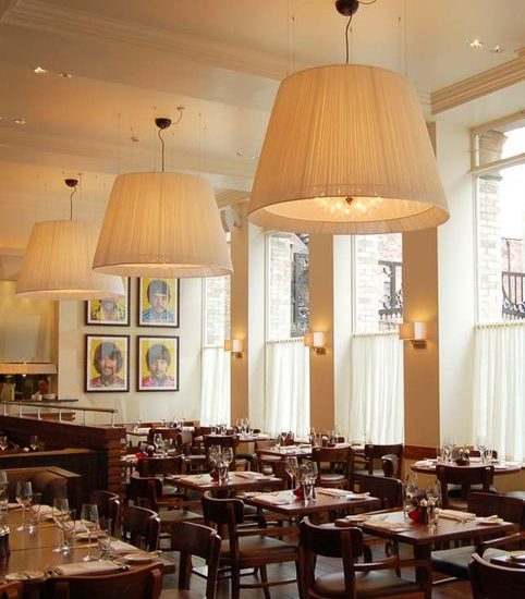 Helles Restaurant mit großen weißen Deckenlampen und dunkelbraunen Holztischen und Stühlen. An der Wand Portraits der Beatles.