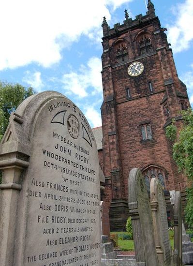 Friedhof mit hellem Grabstein von Eleanor Rigby mit Backsteinkirche im Hintergrund.