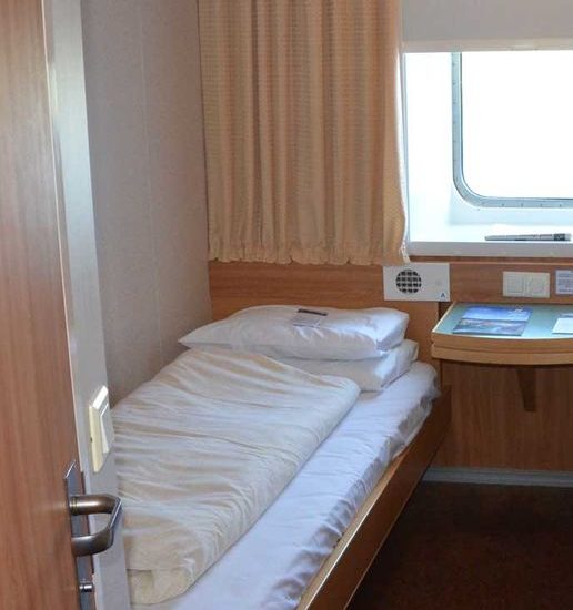 Einzelbett mit weißer Bettwäsche in einer Kabine einer Fähre.