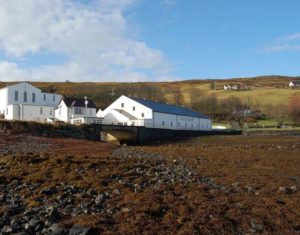 Weiß gestrichene Talisker Distillery mit Seetang im Vordergrund