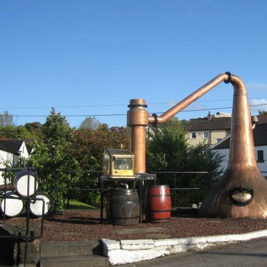 Vor der Auchentoshan Distillery sind eine alte halbierte Brennblase, ein spirit safe und ein paar Fässer dekoriert.