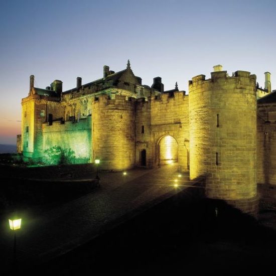 Nachtaufnahme vom beleuchteten Stirling Castle mit mächtigen Wehrtürmen, die den Eingang flankieren.