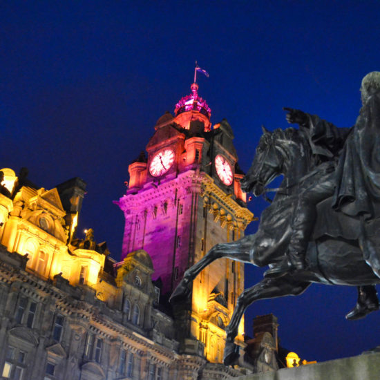 Eine schwarze Reiterstatue steht vor dem festlich farbig angestrahlen Uhrturm des Balmoral Hotels.