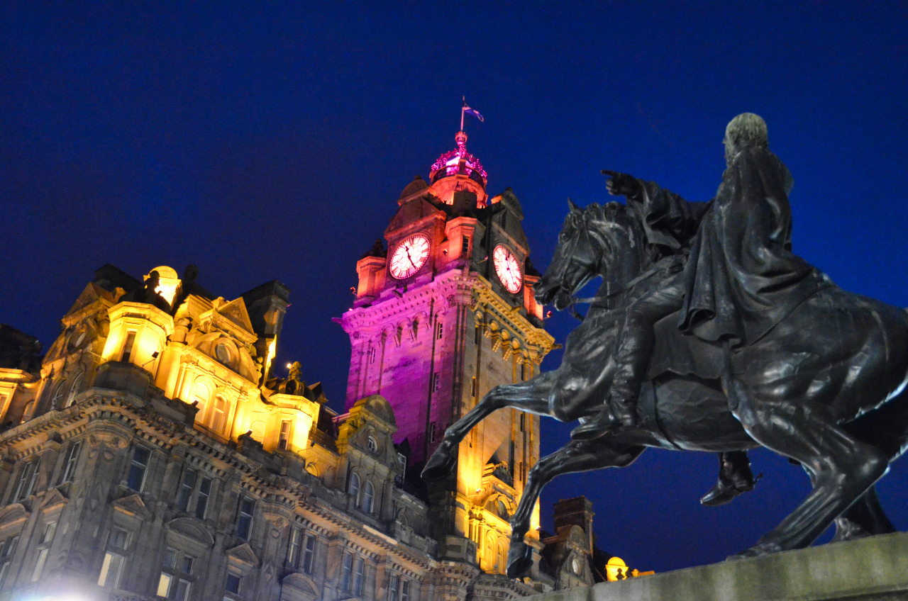 Eine schwarze Reiterstatue steht vor dem festlich farbig angestrahlen Uhrturm des Balmoral Hotels.