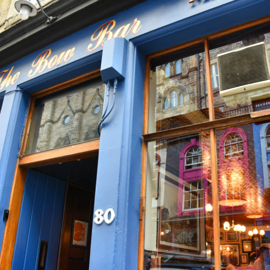 Blaue Fassade der Bow Bar, in dessen Glasfenster sich die gegenüberliegenden Häuser spiegeln.