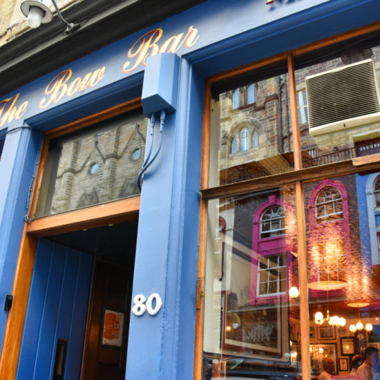 Blaue Fassade der Bow Bar, in dessen Glasfenster sich die gegenüberliegenden Häuser spiegeln.