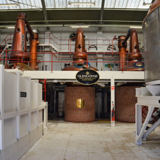 Drei Kupferbrennblasen auf einem gemauerten Sockel bilden den Hintergrund bei einem Blick in das Stillhouse der Whiskydestillerie Glengoyne.