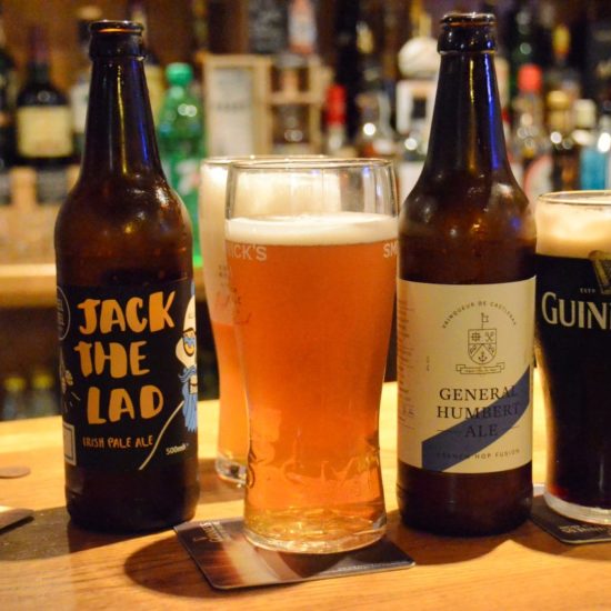 Zwei Flaschen Irish Ale stehen mit drei Biergläsern auf einem Tresen im Pub.