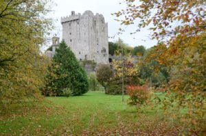 Die Blätter fallen im herbstlichen Park mit dem Wehrturm von Blarney Castle im Hintergrund.