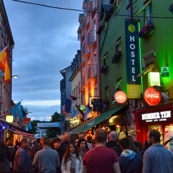 Bunte Straßenszene von Galways Unterhaltungs- und Gastronomiestraße in der Abenddämmerung