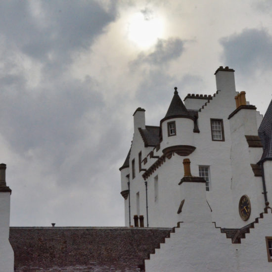 Weiße Giebel und Zinnen eines wehrhaften Schlosses vor einem wolkenbedeckten Himmel.