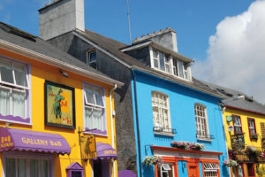 Sehr bunte irische Häuserzeile mit Blumenkisten und Werbeschildern leuchtet in der Sonne.
