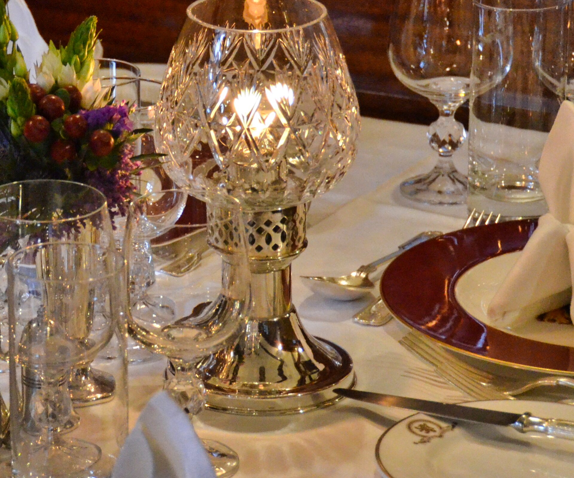 Elegant eingedeckter Tisch mit Silberbesteck, Kristallleuchter und Gläsern. Die Teller mit rotem Rand tragen das Logo des Luxuszugs Royal Scotsman.